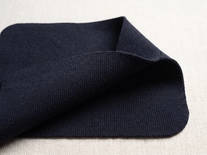 Close-up of dark knitted fabric folded on a pale surface.